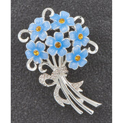 Equilibrium Forget Me Not silver-tone brooch with blue flower bouquet, amber crystal-effect centres and clear crystal-effect bow detail, on dark background