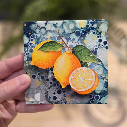Lemon ceramic coaster held in hand showing full lemon design with teal bubble-effect background, outdoors