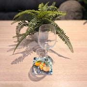 Lemon ceramic coaster on wooden table with wine glass on top beside fern plant