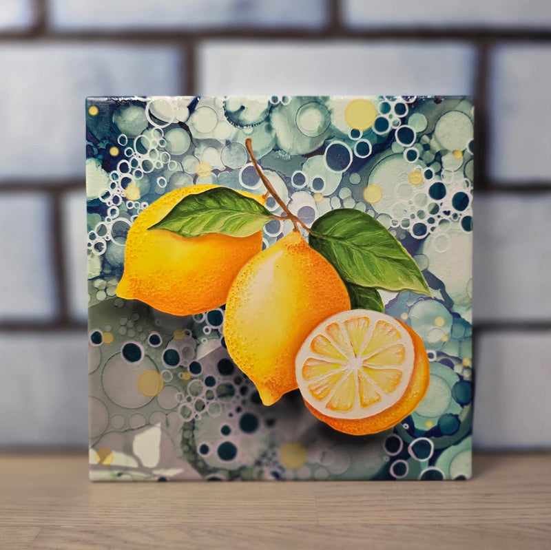 Lemon ceramic trivet standing upright against white tiled wall showing full lemon design with teal bubble-effect background