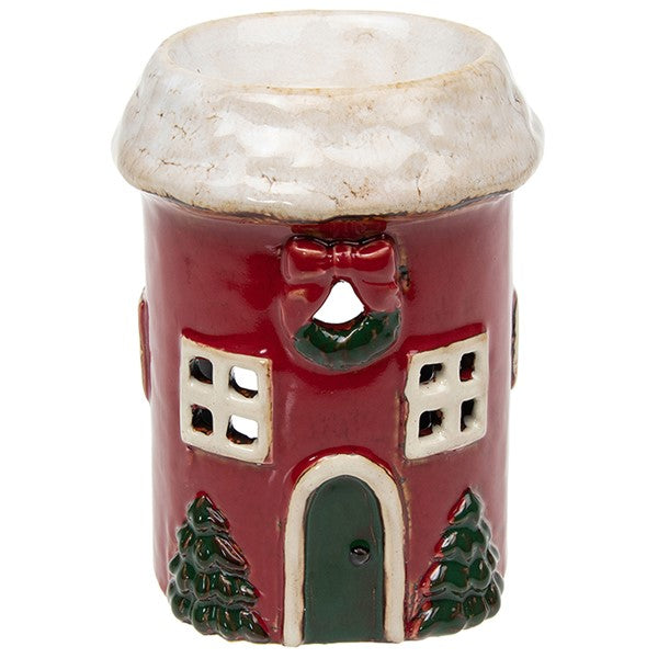 Village Pottery Christmas round cottage wax melt warmer — red cottage with snow-dusted roof, festive wreath with bow, cut-out windows, green arched door, and Christmas trees either side