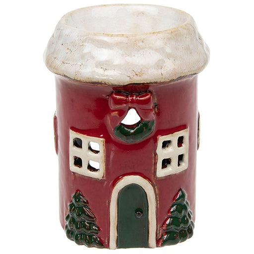Village Pottery Christmas round cottage wax melt warmer — red cottage with snow-dusted roof, festive wreath with bow, cut-out windows, green arched door, and Christmas trees either side