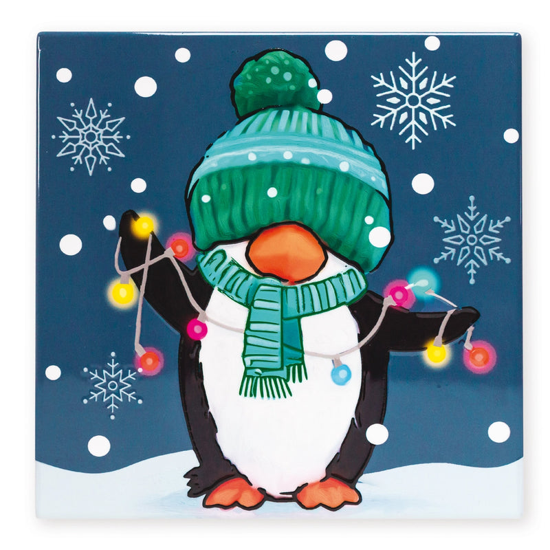 Square Christmas trivet featuring a penguin wearing a bobble hat and scarf, holding a string of colourful Christmas lights, with snowflakes in the background.