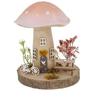 Spring Folk Art Mushroom House ornament with pink pastel cap on wooden log base with miniature bicycle, bench and dried flowers