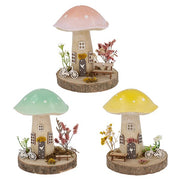 Spring Folk Art Mushroom House ornaments in three pastel colours — pink, green and yellow — with wooden log base, miniature bicycle, bench and dried flower details