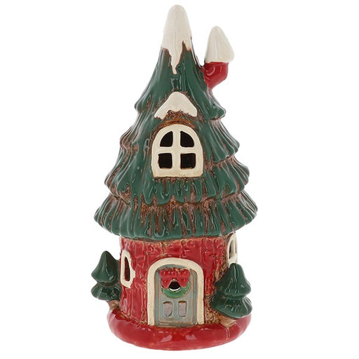 tiered branch roof with snow-tipped peaks and red chimney, arched window, red base with arched door with wreath and small Christmas trees, white background