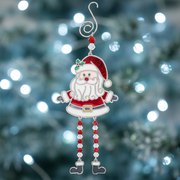A stained glass style Christmas Santa decoration in red with a white curly beard, gold buckle belt, holly detail and dangly red and clear bead legs with boot charms, displayed with cool white bokeh fairy lights