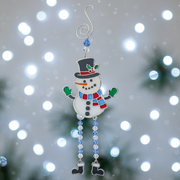 A stained glass style Christmas snowman decoration with a dark blue top hat and holly, red and blue striped scarf, green mittens and dangly blue and clear bead legs with boot charms, displayed with cool white bokeh fairy lights