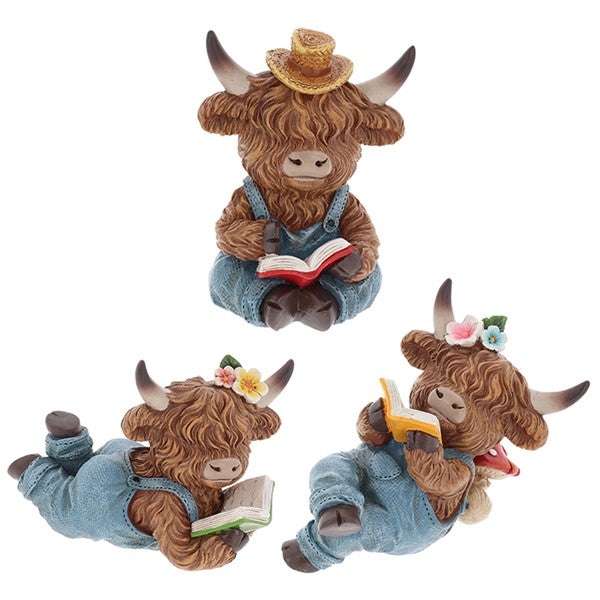  Three highland cow reading figurines in denim dungarees — one sitting with straw hat reading a red book, two lying down with flower accessories reading yellow and green books