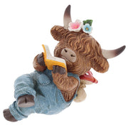 Highland cow reading figurine lying down in denim dungarees with flower hair accessories, reading a yellow-covered book, shaggy fur and curved horns