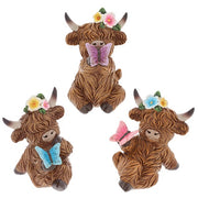 Garden Bloom Highland Cow ornaments in three butterfly colours — purple, blue and pink — each with a floral crown, on a white background
