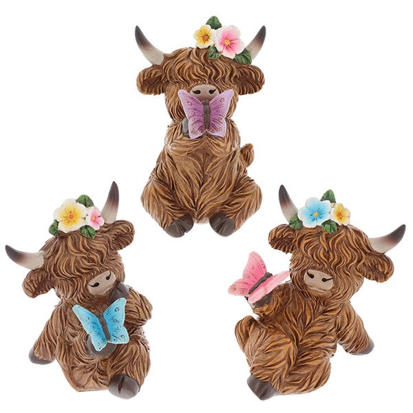 Garden Bloom Highland Cow ornaments in three butterfly colours — purple, blue and pink — each with a floral crown, on a white background
