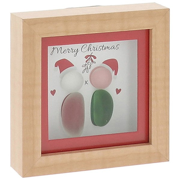 A small square natural wood box framed pebble art picture with two pebble figures wearing red Santa hats standing beneath a sprig of mistletoe with a kiss "x" and red hearts, and the sentiment "Merry Christmas"