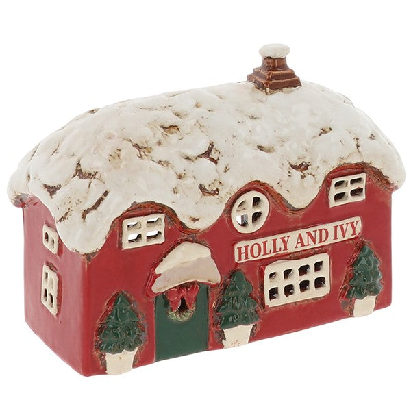 Village Pottery Holly & Ivy Pub Christmas tealight holder, red two-storey pub with snow-laden thatched roof, brown chimney, wreath-decorated green door, two dark green topiary trees and Holly and Ivy lettering across the front