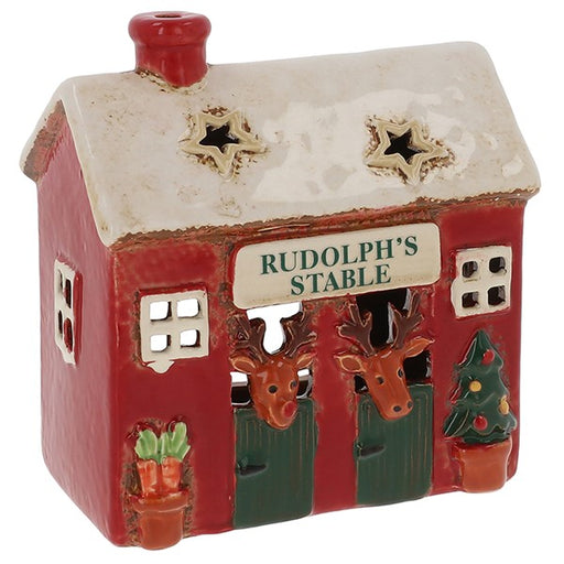 Village Pottery Rudolph's Stable Christmas tealight house, red building with snow-dusted roof, two star cutouts, two reindeer over green stable doors, pot of carrots and Christmas tree, white background