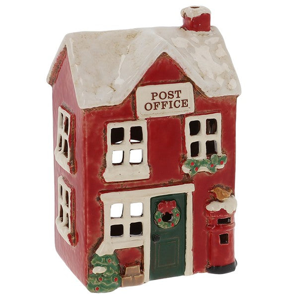 Village Pottery Christmas post office tealight house, red two-storey building with snow-dusted roof, green door with wreath, holly garland, red post box with robin perched on top and Christmas tree, white background