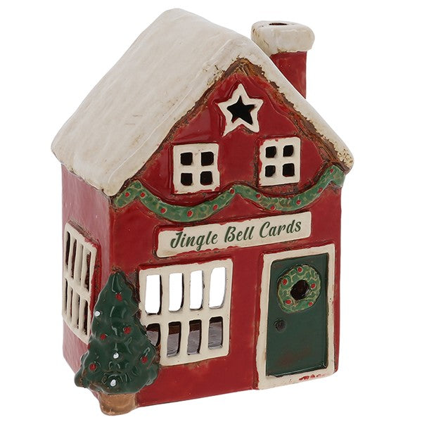 Village Pottery Christmas card shop tealight house, red building with snow-dusted roof, star cutout in gable, garland, wreath on green door and Christmas tree, white background