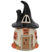 Village Pottery witch's round house tealight holder with swooping black hat roof, side chimney, orange-framed windows, little door with broom, and miniature pumpkins at the base