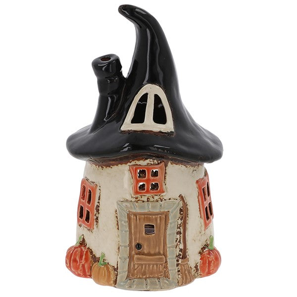 Village Pottery witch's round house tealight holder with swooping black hat roof, side chimney, orange-framed windows, little door with broom, and miniature pumpkins at the base