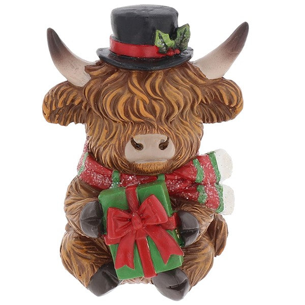 Merry Christmas Coos mini highland cow figurine wearing a black top hat with holly, holding a wrapped green gift with a red bow