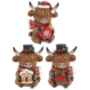 Three Merry Christmas Coos mini highland cow figurines — holding a bauble, a gingerbread house, and a wrapped present, each with shaggy fur detail and curved horns, 5 x 4.5 x 7cm