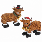 Two Merry Christmas Coos in Boots mini highland cow figurines — one with a black top hat and one with a red Santa hat, both with holly wreaths, gold bows and black boots with white fluffy trim