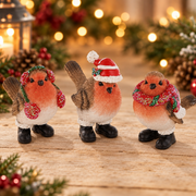 Three Christmas Robin in Boots small decorations displayed together with warm golden bokeh fairy lights background