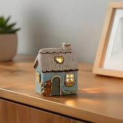 Village Pottery Garden Thatched Blue Cottage tealight holder glowing warmly on a wooden sideboard