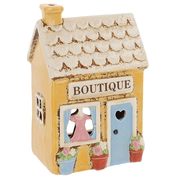 Village Pottery Boutique ceramic tea light holder, angled view showing blue heart-cut door, shop window with pink dress display and flower pots