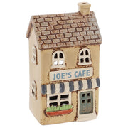 Village Pottery ceramic Joe's Cafe tea light holder, warm sandy two-storey building with grey brick-effect roof, grey and white striped awning, Joe's Cafe signage and terracotta window box