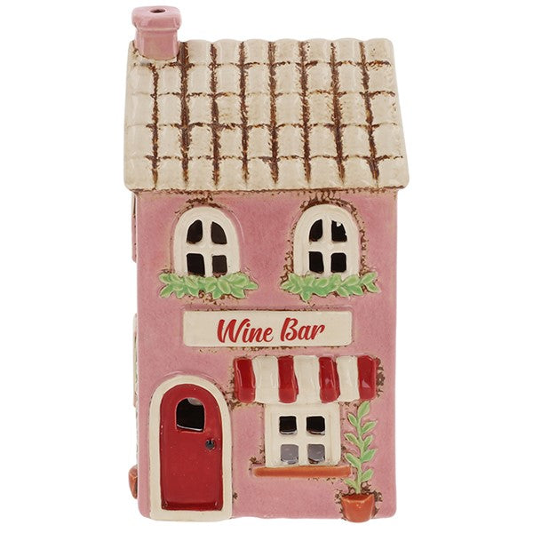 Village Pottery ceramic wine bar tea light holder, pink two-storey building with tiled roof, red arched door, red and white striped awning and window boxes with greenery