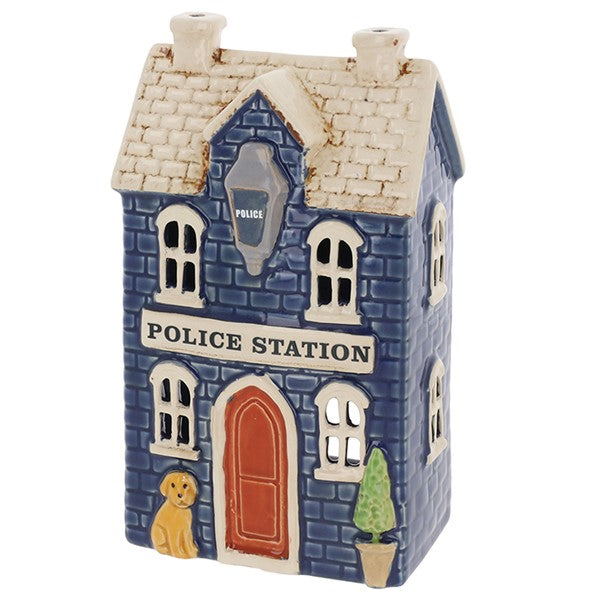Angled view of Village Pottery police station tea light holder showing twin chimneys, arched windows and potted topiary tree