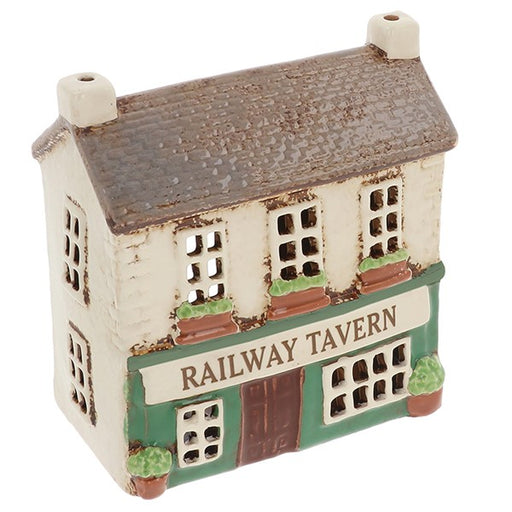 Village Pottery Railway Tavern tealight holder, cream two-storey ceramic pub with brown tiled roof, two cream chimneys, green fascia with Railway Tavern sign, brown door, windows with white frames, terracotta flower boxes and round topiary trees in terracotta pots, white background