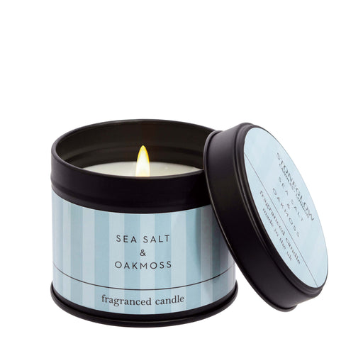 Stoneglow Modern Classics Sea Salt and Oakmoss black candle tin with pale blue label, lid resting against tin, wick lit