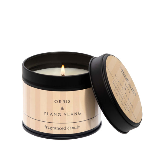 Stoneglow Modern Classics Orris and Ylang Ylang black candle tin with warm blush label, lid resting against tin, wick lit