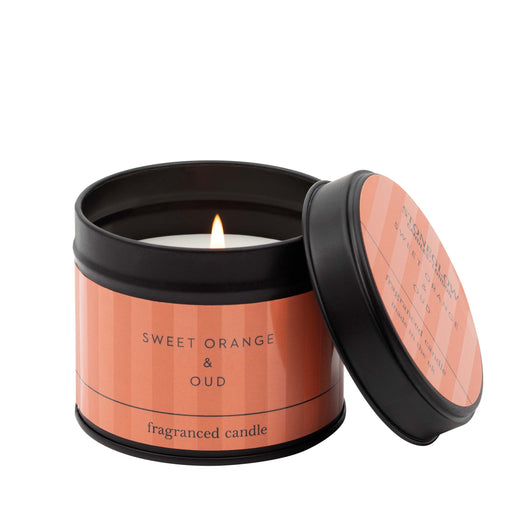 Stoneglow Modern Classics Sweet Orange and Oud black candle tin with coral label, lid resting against tin, wick lit