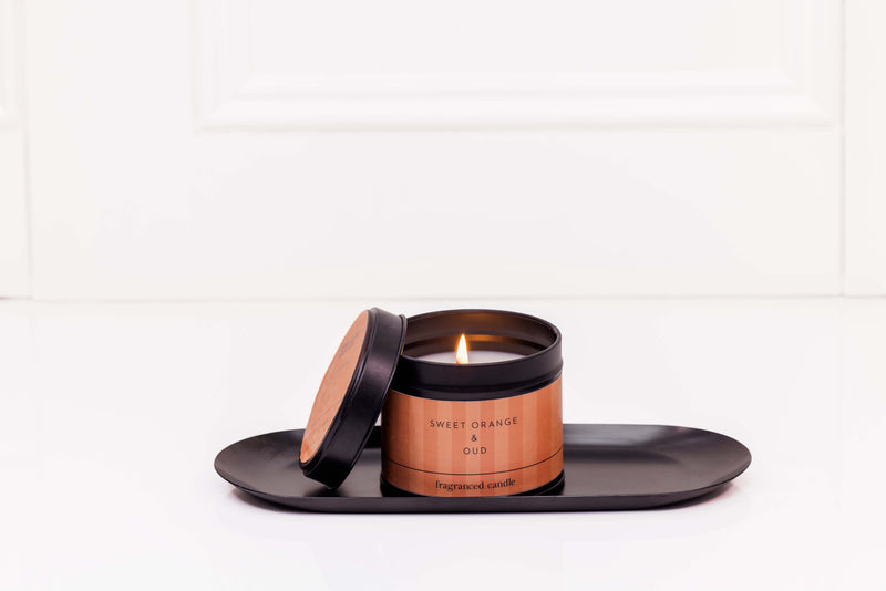 Stoneglow Modern Classics Sweet Orange and Oud candle tin with lit wick styled on black tray