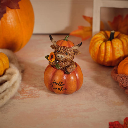 Highland cow figurine sitting inside a pumpkin wearing a pumpkin hat and holding a sunflower, with "Hello Pumpkin" inscription on the front, 9.5 x 9 x 12.5cm