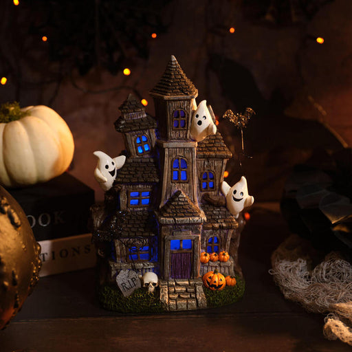 Tall Halloween haunted house decoration with friendly ghosts, jack-o'-lanterns, bat and skull details, with multicoloured LED glowing windows and door, 17.5 x 13 x 25.5cm