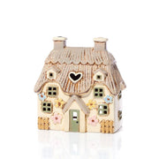 Front view of cream stoneware floral cottage tealight holder showing sage green door, pastel flowers and thatched roofline, Stoneware Country Cottage Collection