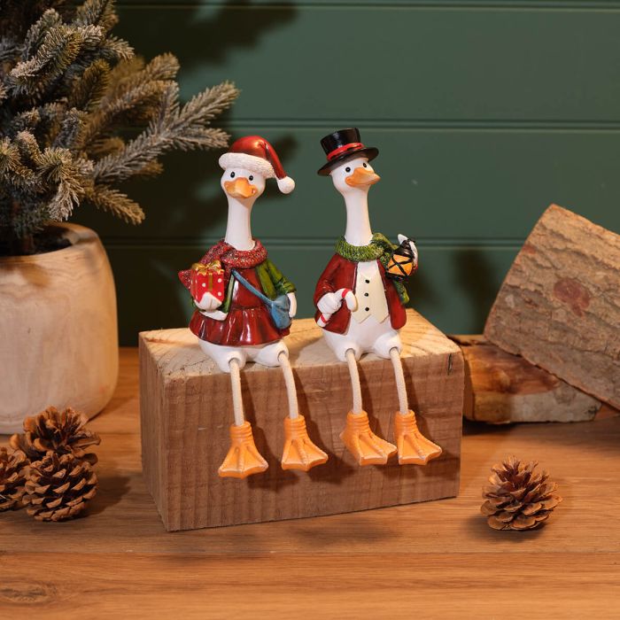 Mr and Mrs Christmas duck decorations with dangling legs sitting on a wooden block with pine cones and Christmas tree in background