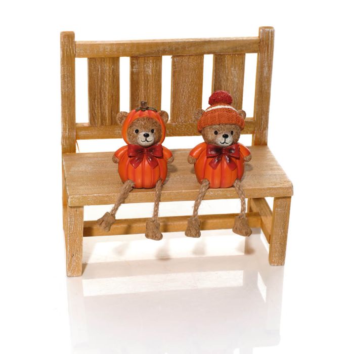Two pumpkin bear shelf sitter ornaments seated on a wooden bench, one wearing a pumpkin hood and one wearing a knitted bobble hat with dangly rope legs, white background