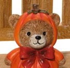 Pumpkin bear shelf sitter ornament wearing a pumpkin hood with red bow and dangly rope legs, close-up detail