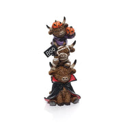 A resin triple stacking highland cow Halloween figurine on a white background — a vampire cow at the bottom in a black and red cape, a mummy cow in the middle holding a BOO sign, and a pumpkin cow at the top in a purple outfit with two jack-o'-lanterns on its horns