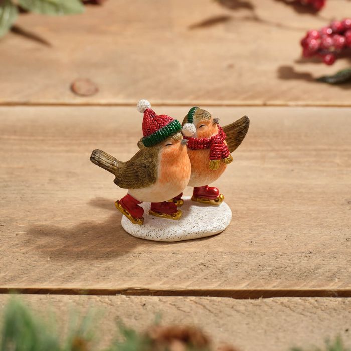 Resin ice skating robin pair Christmas ornament with red and green hats and scarves, styled on wooden surface with red berry branches