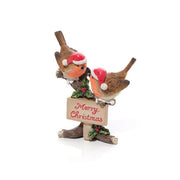 A resin Christmas robin pair figurine with red and white Santa hats, perched on a rustic tree stump with a Merry Christmas sign in red lettering and holly berry detail, on a white background