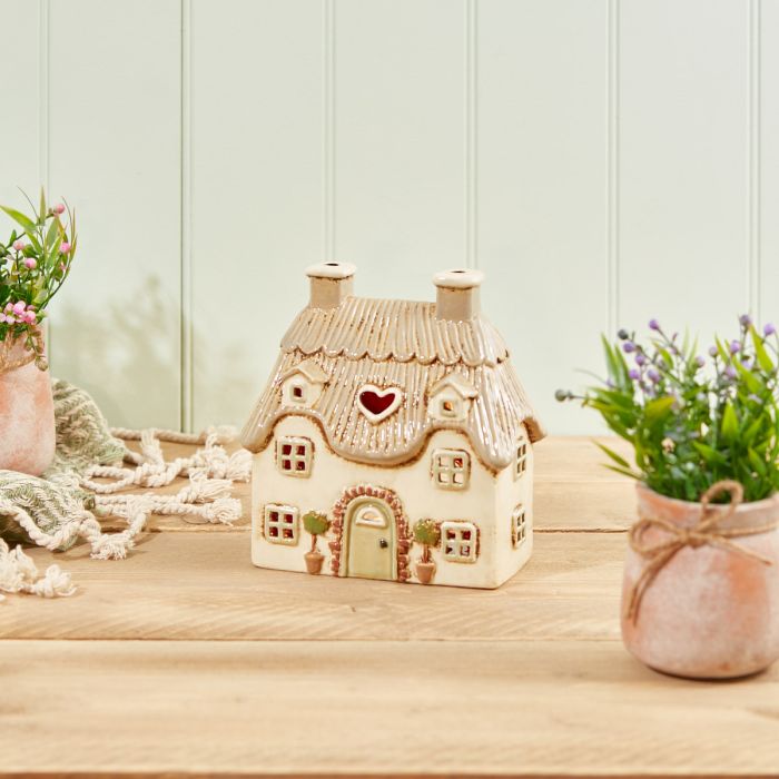 Cream stoneware thatched cottage tealight holder with heart cutout, twin chimneys and potted topiary trees, Stoneware Country Cottage Collection