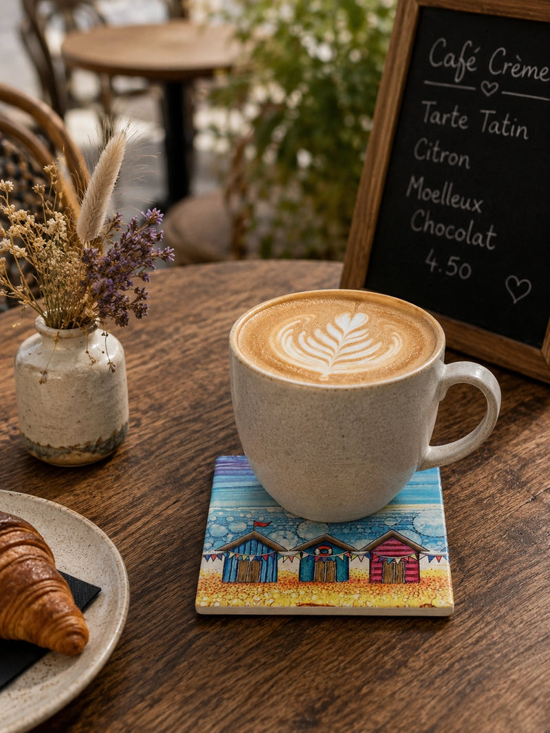 Beach Hut and Bunting ceramic coaster on wooden café table with latte art coffee mug and croissant