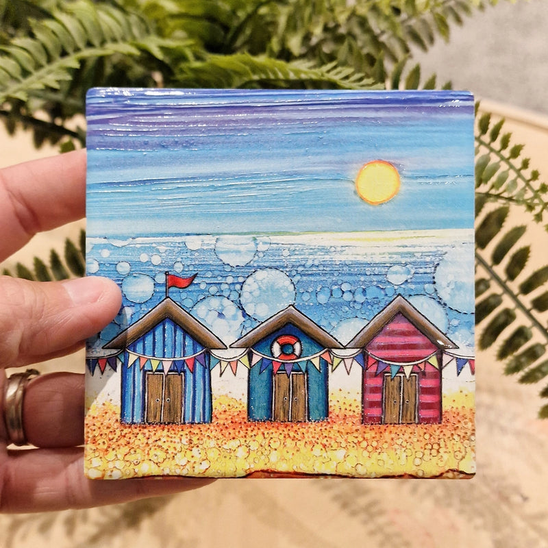 Beach Hut and Bunting ceramic coaster held in hand beside fern plant showing full beach hut and bunting design