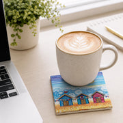 Beach Hut and Bunting ceramic coaster on white desk with latte art coffee mug, laptop, notebook and plant